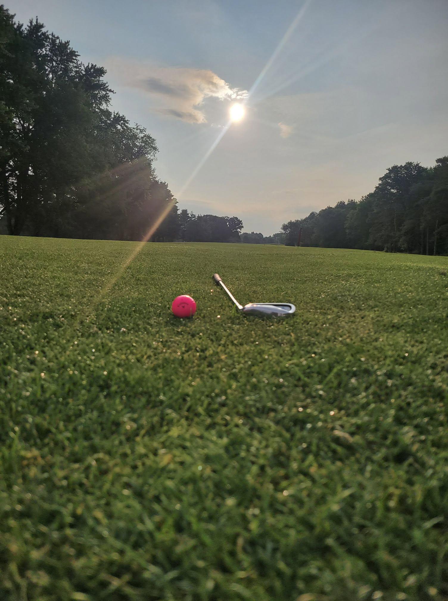 A golf ball and club resting on the fairway at sunrise